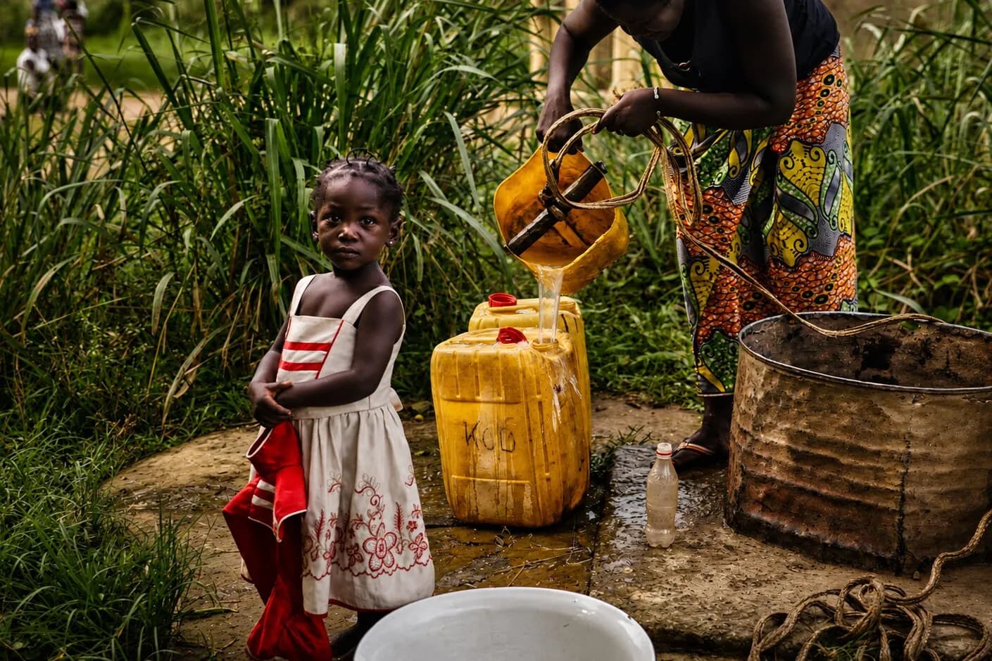 A girl beside yellow jugs as clean water is poured, Central African Republic